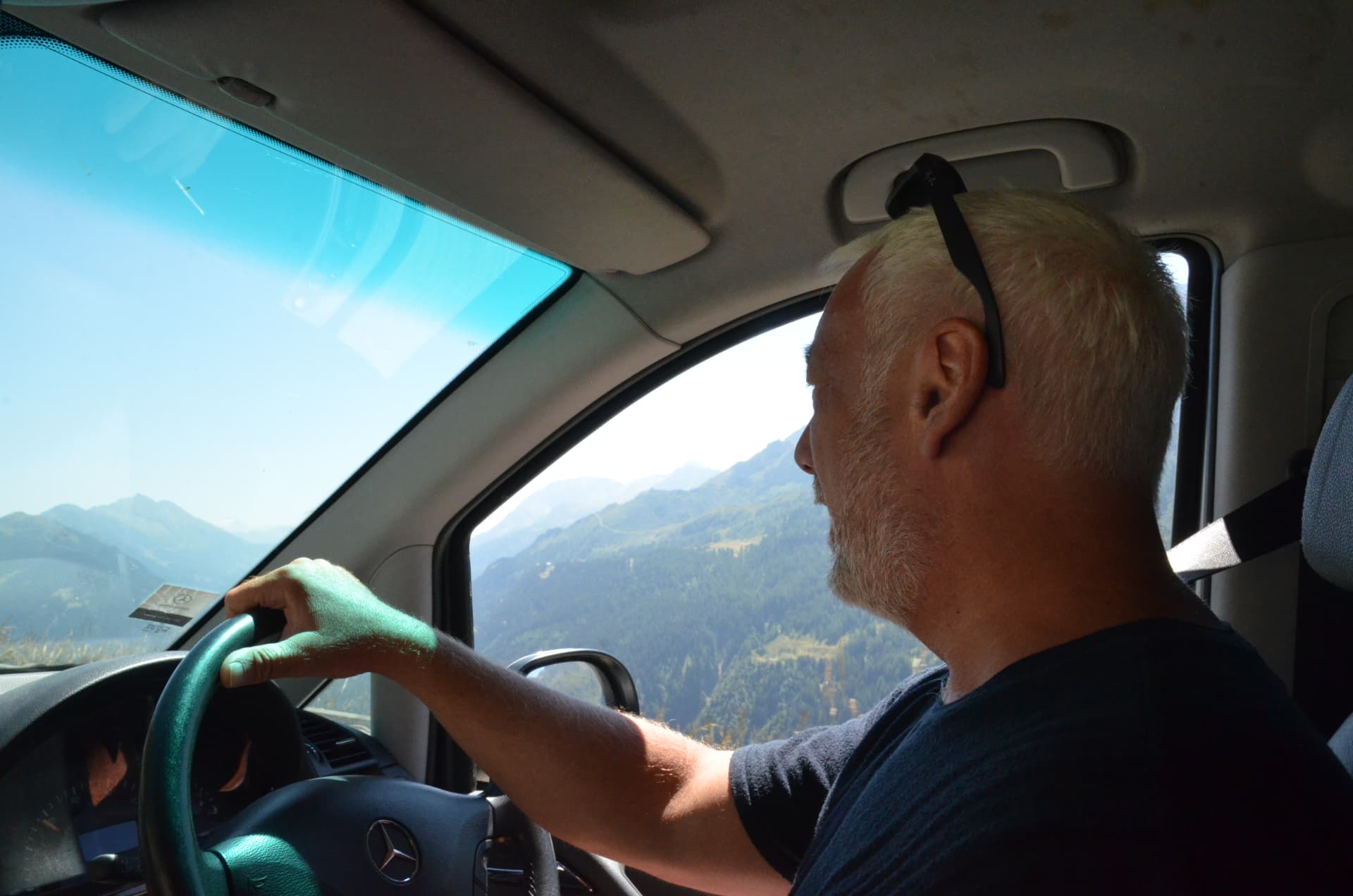 Dan Mills driving through a mountain pass, one hand on the wheel, valley visible through the window