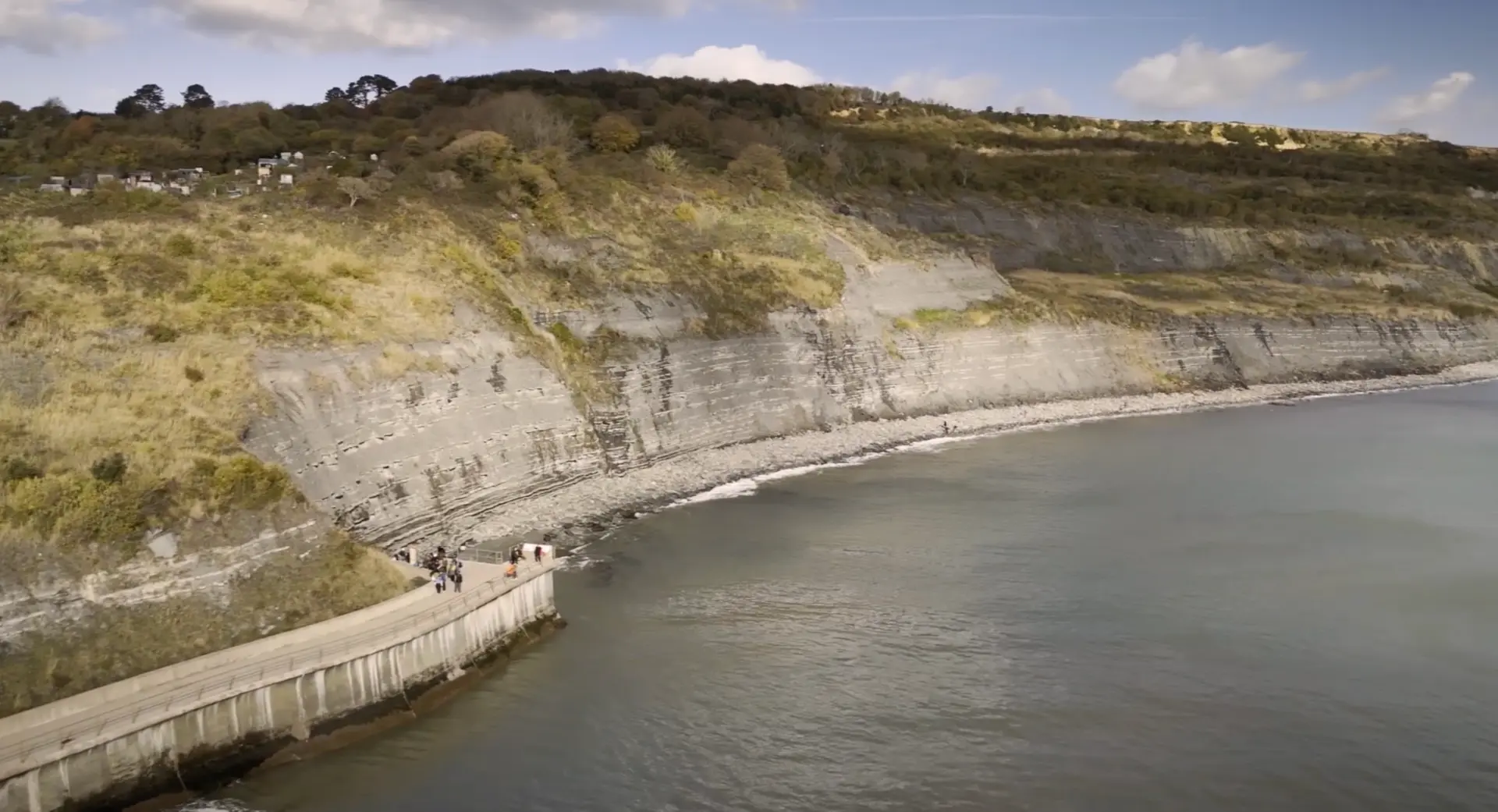 Aerial view of the Jurassic Coast, with layered cliffs above a pebble beach and a sea wall