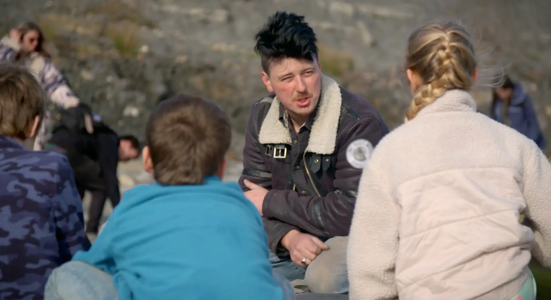A palaeontologist sitting outdoors on the Jurassic Coast talking with a group of school children